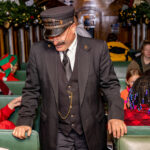 Train conductor walking through the train wearing a Polar Express conductor hat.