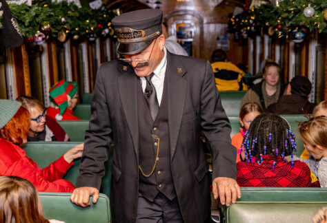 Train conductor walking through the train wearing a Polar Express conductor hat.